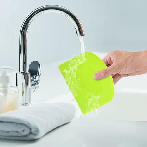 Hand holding green sponge under running faucet